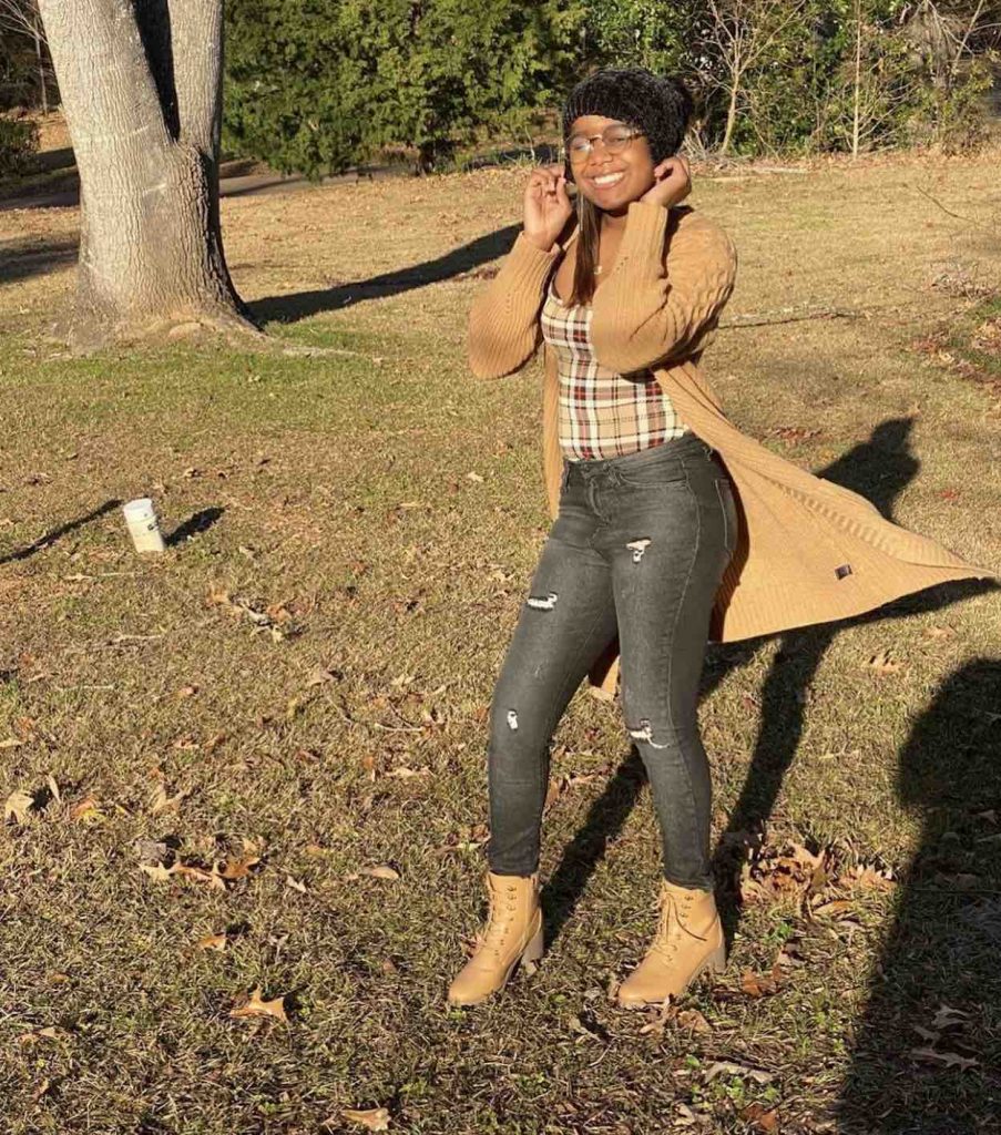 Cambria poses outside in jeans, brown boots and a black hat. 