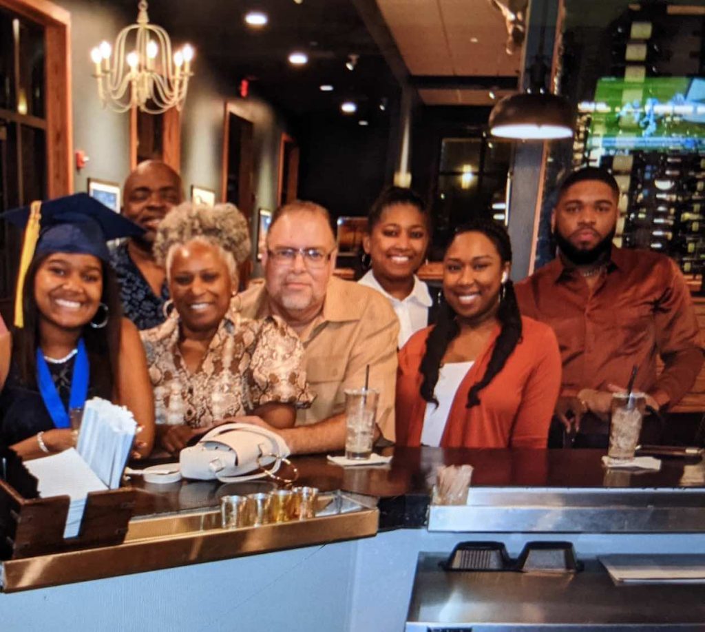 Cambri, wearing a graduate cap, is pictured with her family at a restaurant.