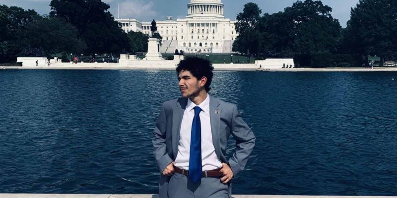Andy Flores stands in a suit and tie in Washington DC in front of the Capitol Building.