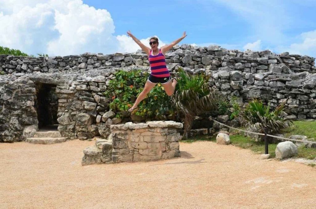 Jori is wearing shorts and a striped tank top as she jumps in the air on a trip to Mayan Ruins in Tulum, Mexico.