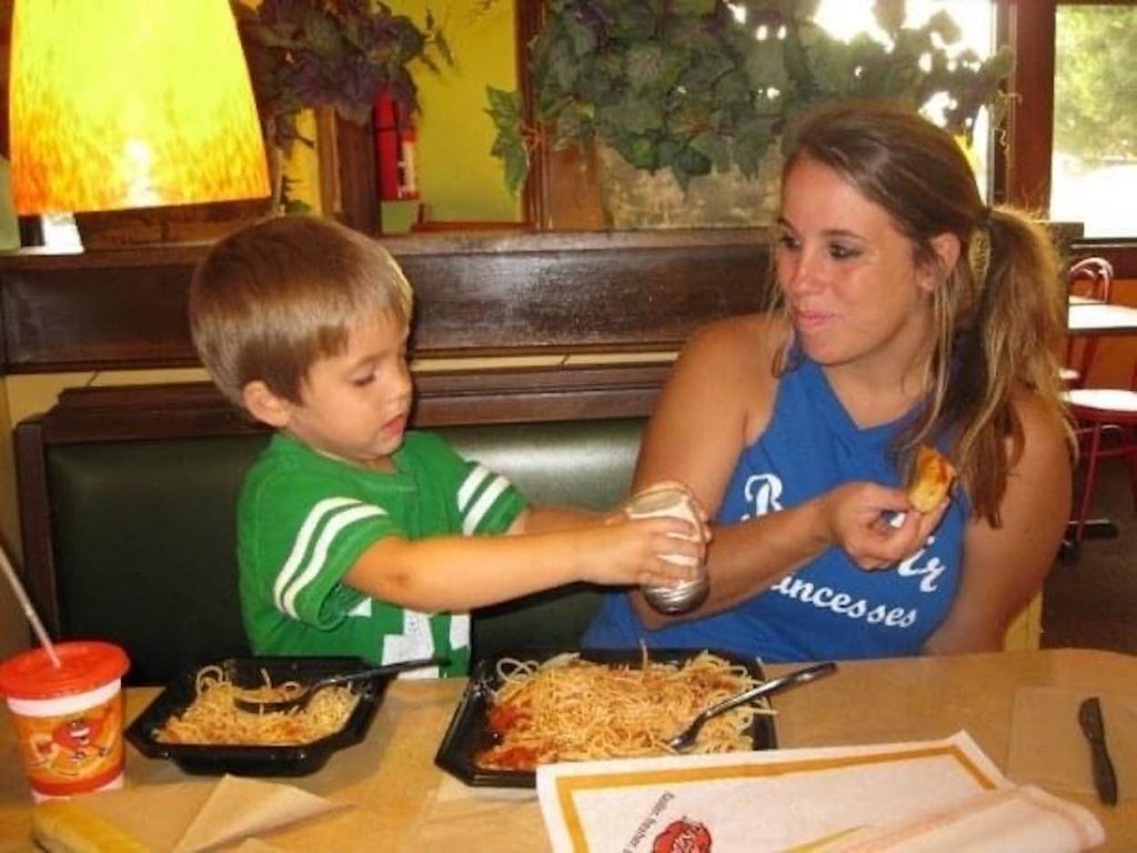 Jori is in a blue shirt and Joshua is wearing a green shirt as they eat pasta.