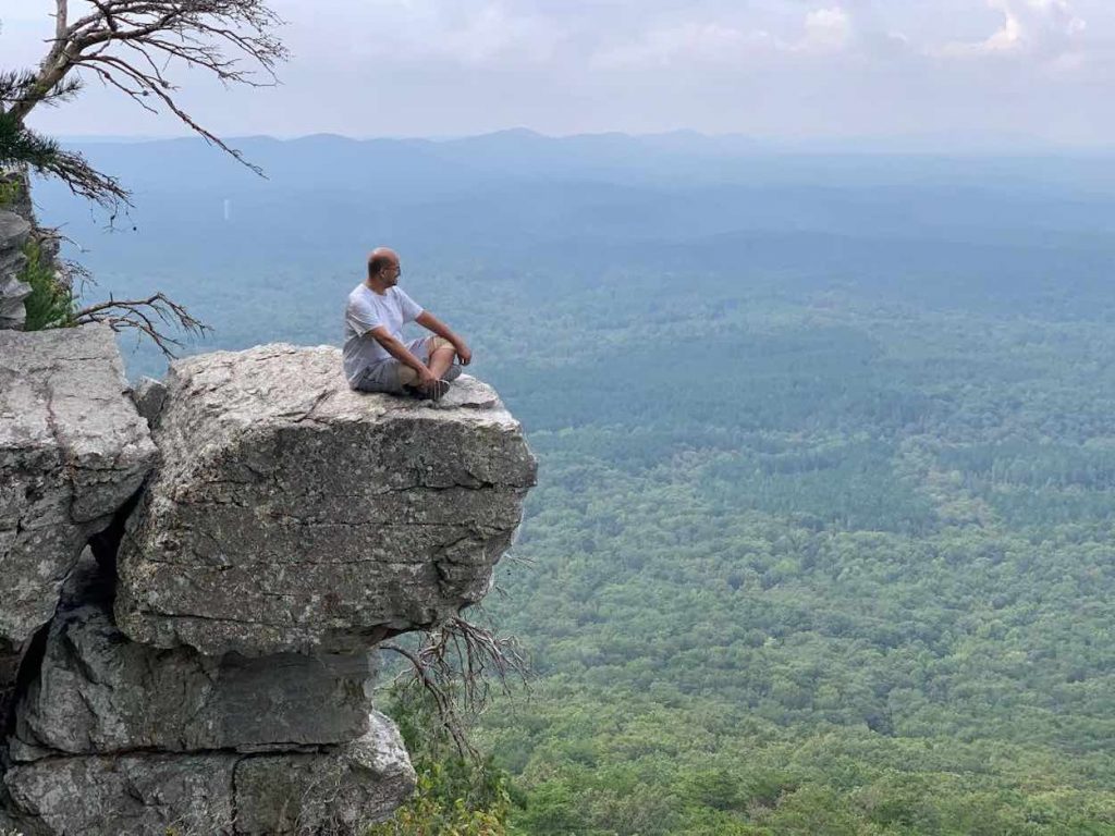 Abdullah sits on a large rock overlooking a mountain view with blue skies.