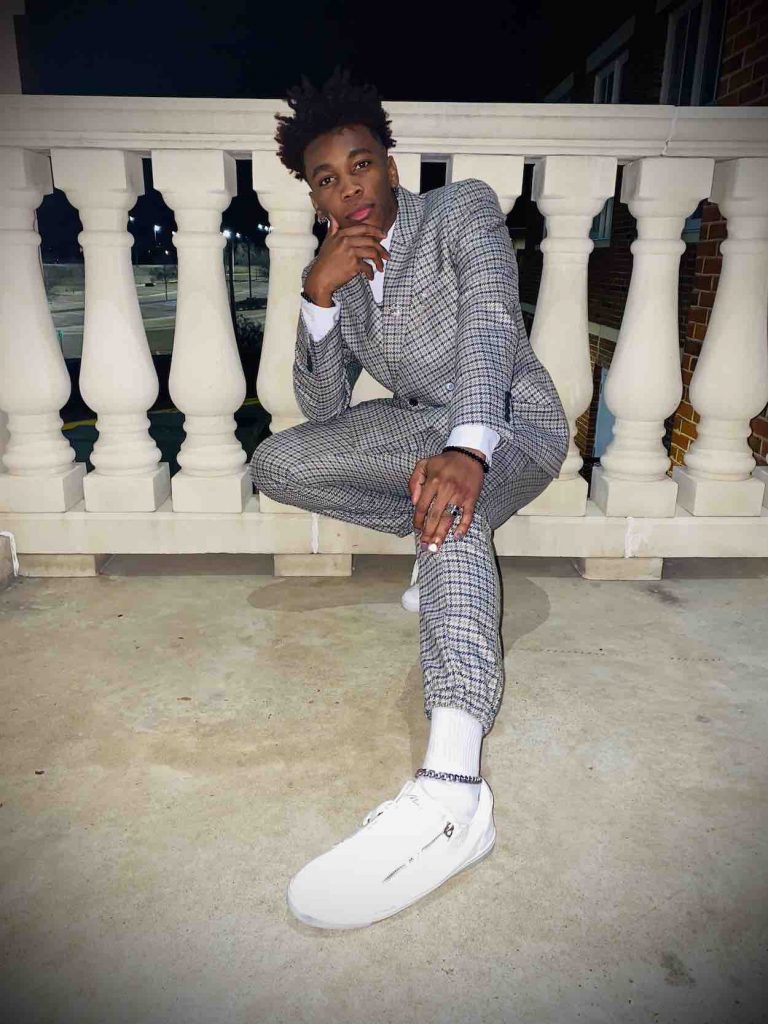 Cellas poses in a gray suit and white sneakers.