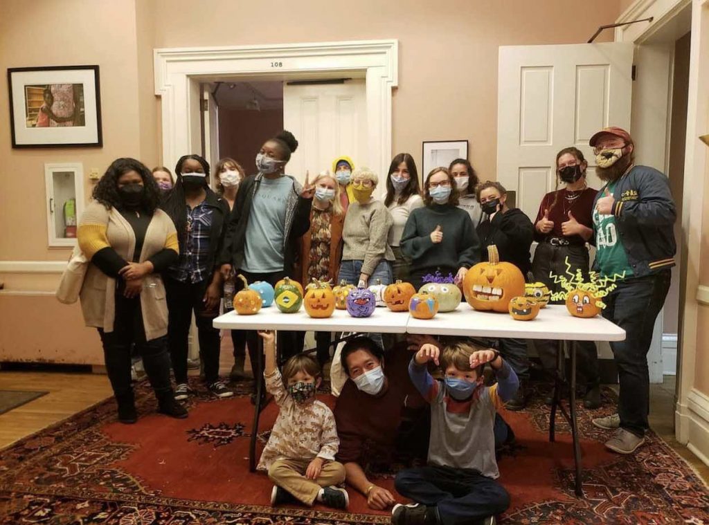 A group of people stand in front of a folding table with decorated pumpkins on it. 