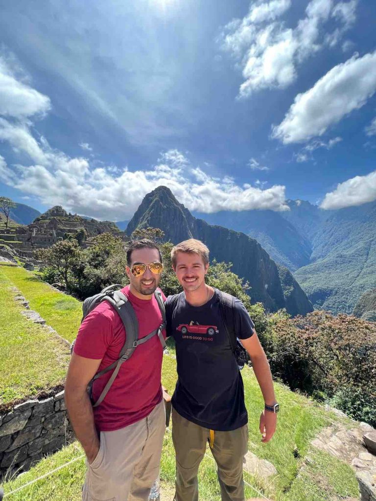 Two men in t-shirts and khakis stand in front of mountain. 