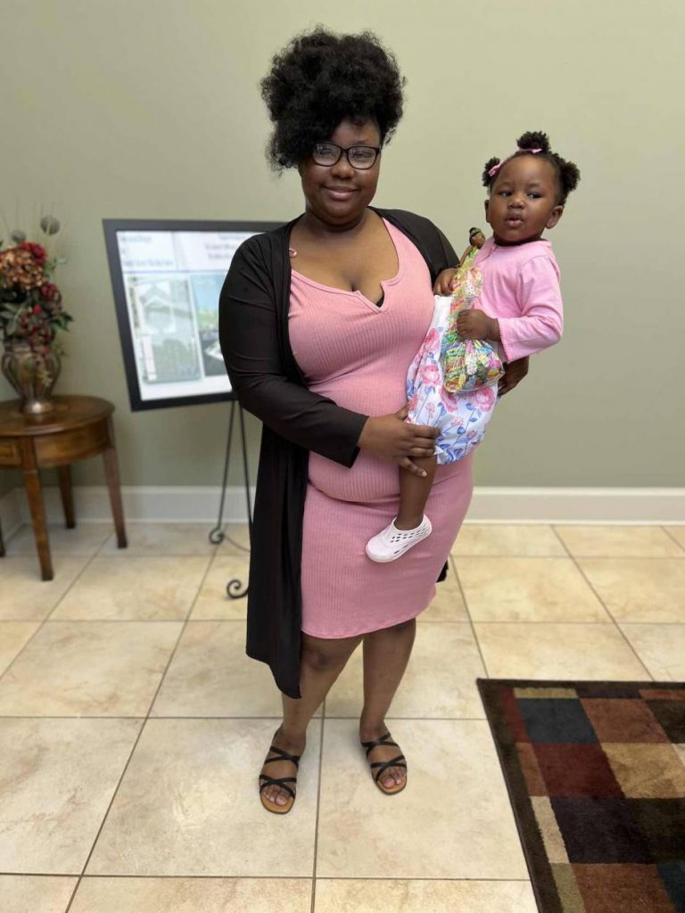 Casiah is wearing a pink dress holding her daughter who is wearing pink. 