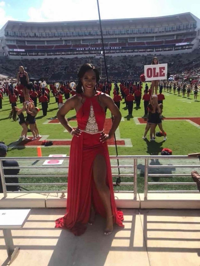Orianna stands in a red formal dress in front of the football field. 