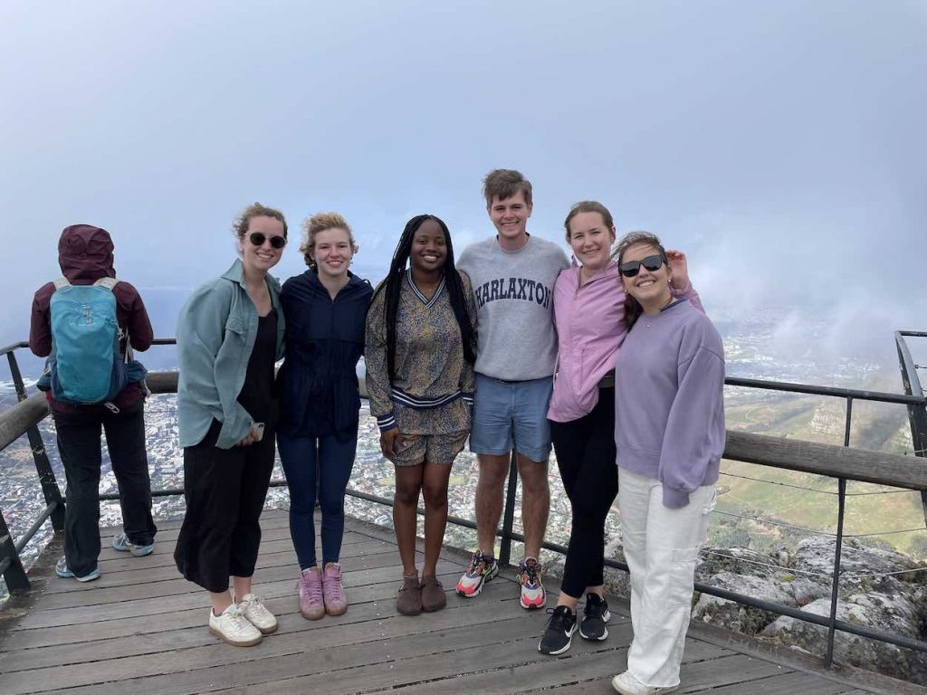 A group of men and women stand on an observation point overlooknig a mountainous area. 