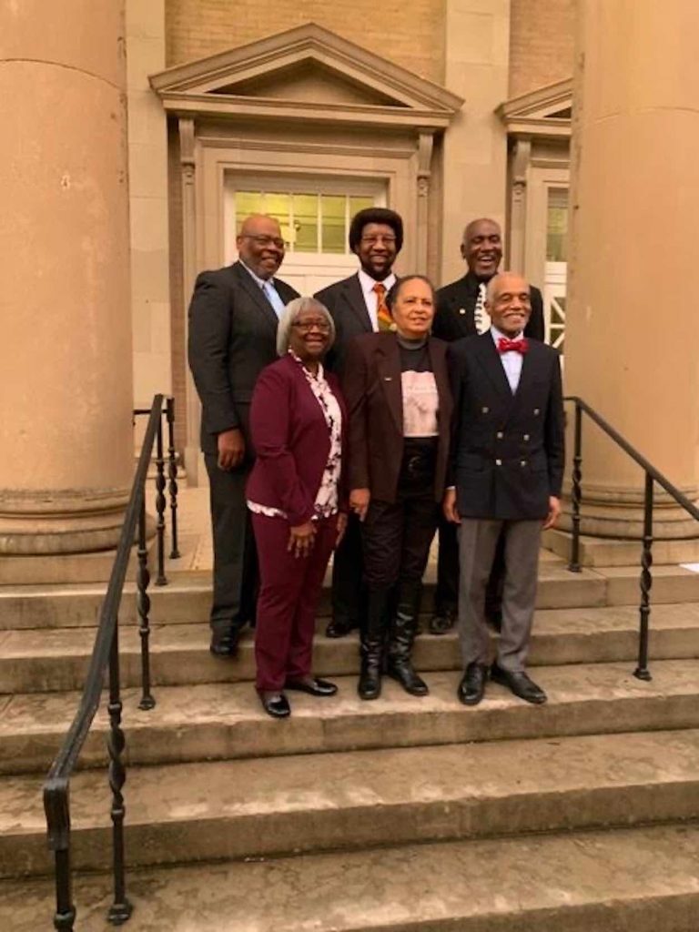 Six African American individuals stand on steps in front of an academic building. 