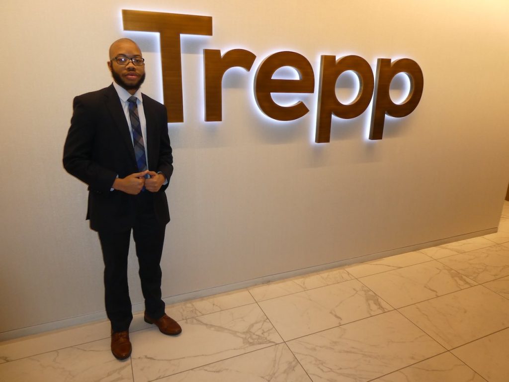 Jaylin stands in a dark suit by a wall with the Trepp logo on it.