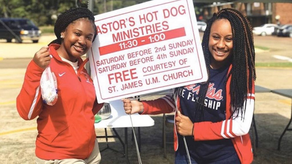 Two girls hold a sign outside.