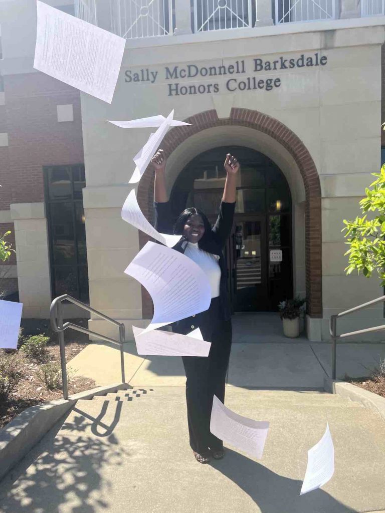 Moore wears a back sweater and pants as she throws the papers of her dissertation in the air in celebration of her completion. 