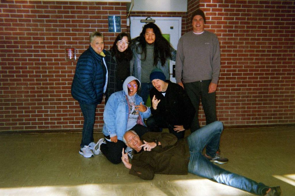 Sandip poses in the middle with several other people in front of a brick wall. 