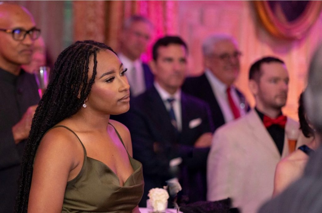 Jilkiah wears a formal green dress in a room with other people at an event.