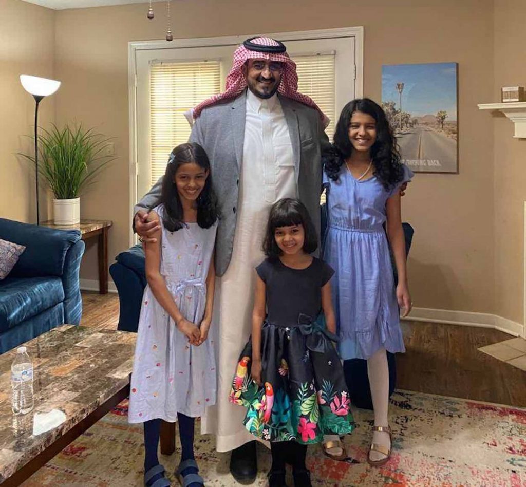 Abdullah stands in a white gown and traditional Arab headdress with three daughters in front of him.