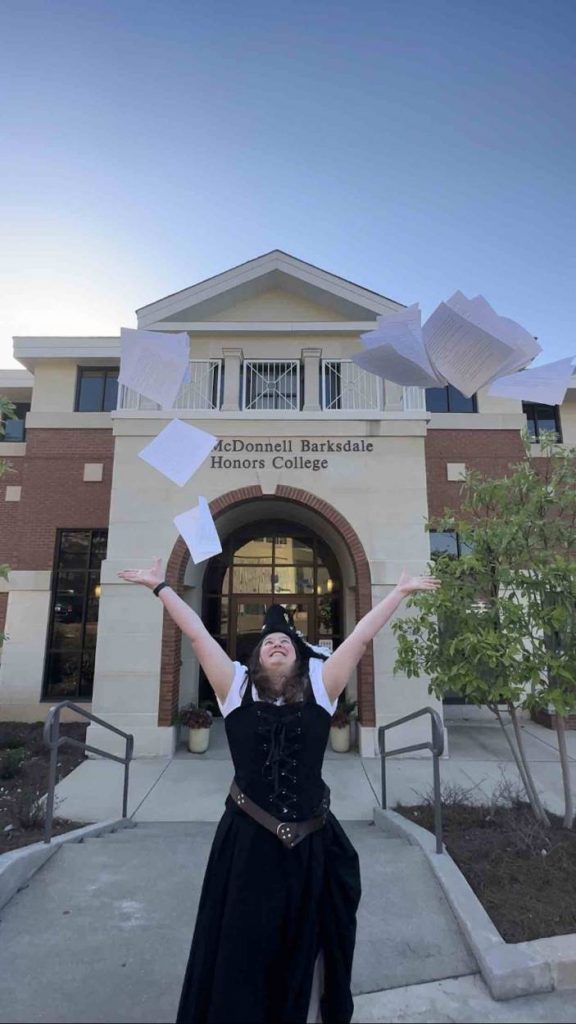 Harris celebrates in a black dress by by throwing papers in the air in front of the Honors College.