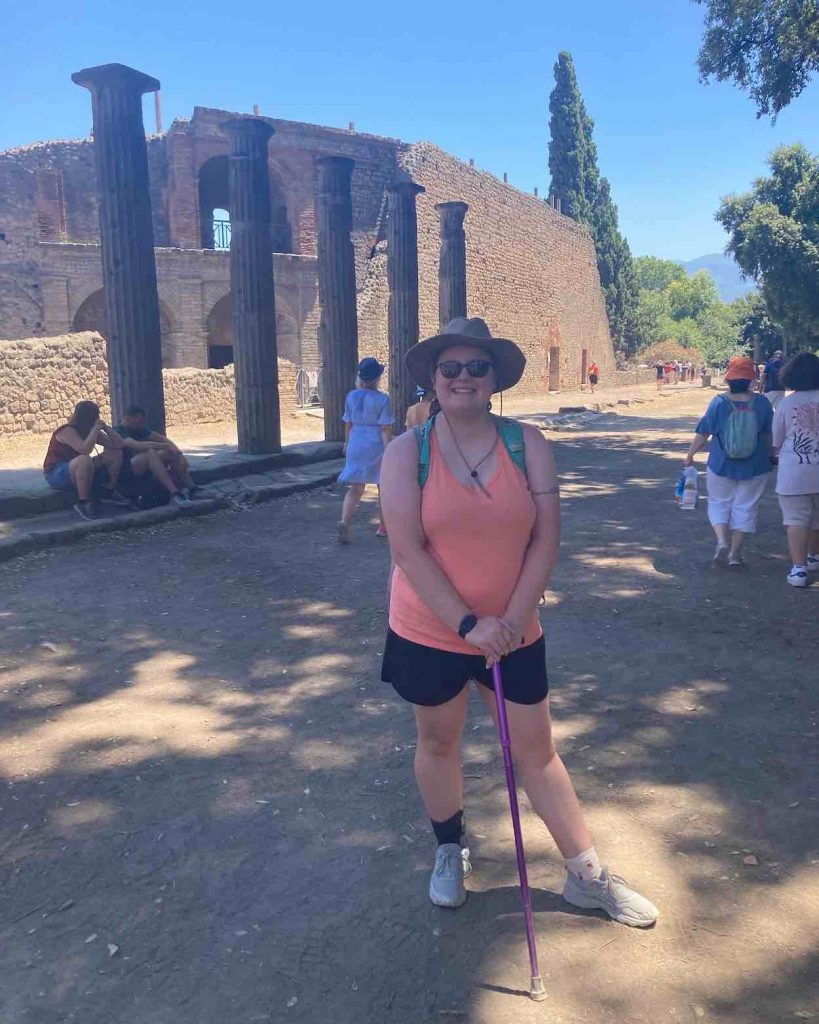 Harris stands in black shorts and a peach tank top in front of ancient ruins.