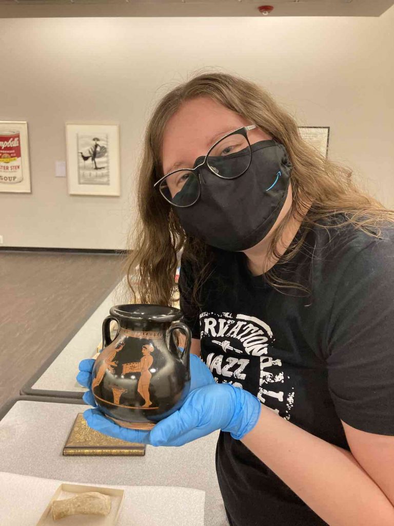Harris wears a mask and holds a vase in a Museum.