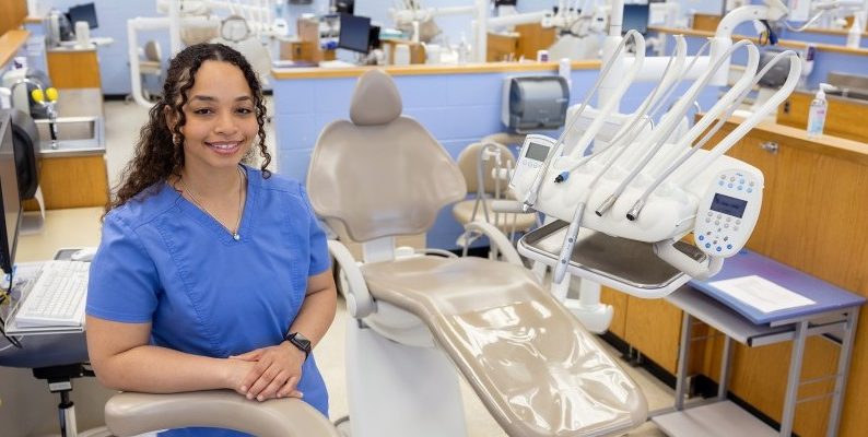 Malita Chaffier stands in blue scrubs in front of a dental chair.